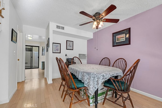 dining area with baseboards, visible vents, light wood finished floors, ceiling fan, and a textured ceiling