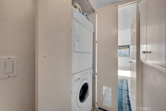 washroom featuring laundry area, a textured wall, stacked washer / drying machine, and a textured ceiling