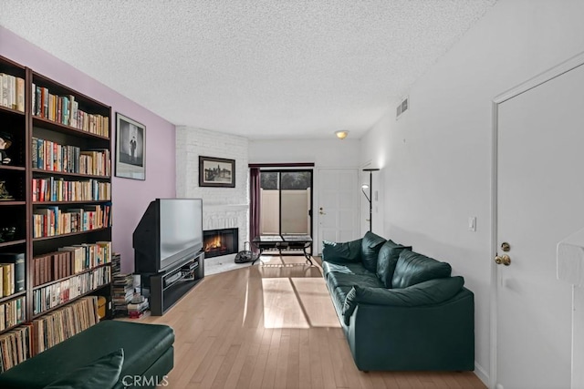 living room featuring visible vents, wood-type flooring, a textured ceiling, and a fireplace