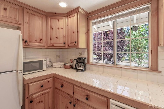 kitchen featuring backsplash, tile countertops, white appliances, and light brown cabinetry