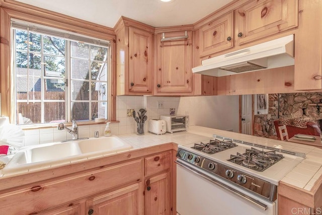 kitchen featuring range with gas stovetop, a sink, tile counters, under cabinet range hood, and backsplash