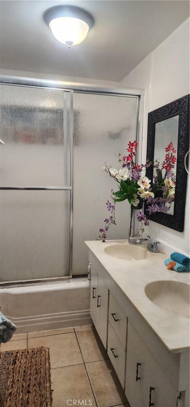 bathroom with tile patterned flooring, combined bath / shower with glass door, double vanity, and a sink