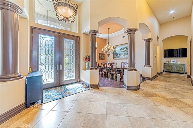 entryway featuring french doors, arched walkways, a high ceiling, light tile patterned floors, and ornate columns