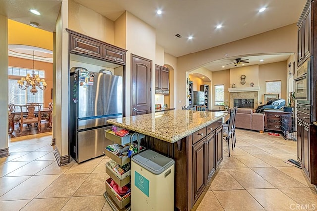 kitchen with light tile patterned flooring, appliances with stainless steel finishes, light stone countertops, and arched walkways