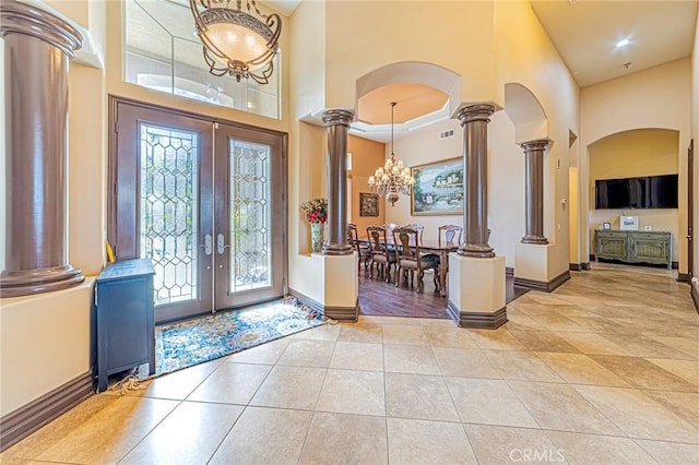 entryway with decorative columns, french doors, arched walkways, a high ceiling, and light tile patterned flooring