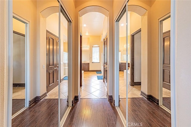 corridor with baseboards, arched walkways, and wood finished floors