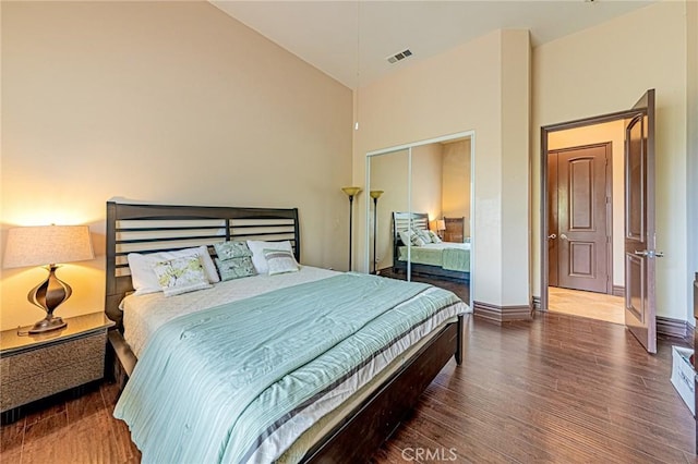 bedroom with visible vents, baseboards, wood finished floors, a closet, and high vaulted ceiling