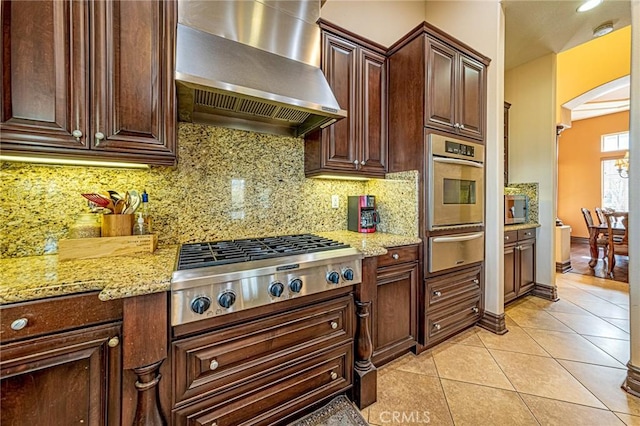 kitchen with light tile patterned floors, decorative backsplash, appliances with stainless steel finishes, a warming drawer, and wall chimney exhaust hood