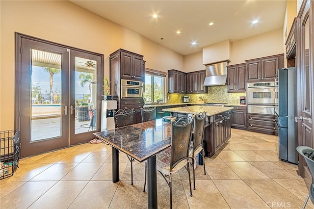 kitchen with a center island, wall chimney range hood, light tile patterned floors, appliances with stainless steel finishes, and french doors