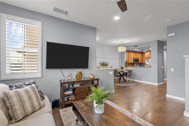 living room with baseboards, wood finished floors, visible vents, and ceiling fan