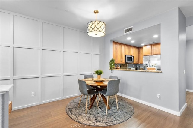 dining room with light wood-type flooring, visible vents, recessed lighting, a decorative wall, and baseboards