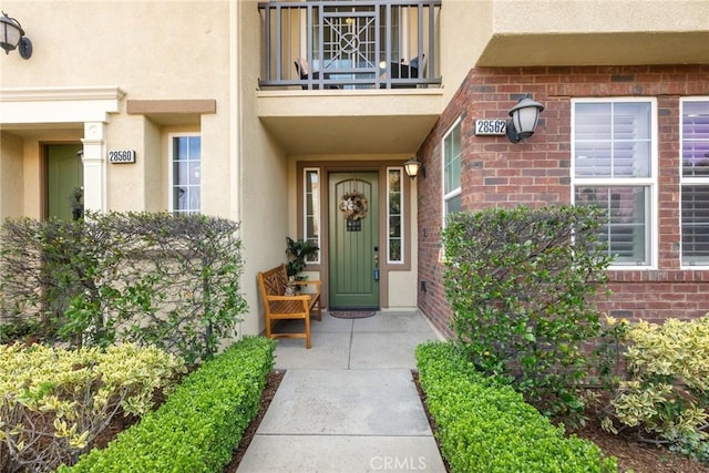 doorway to property with a balcony, brick siding, and stucco siding