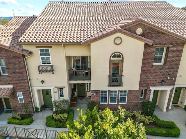 mediterranean / spanish home with brick siding, stucco siding, and a tile roof