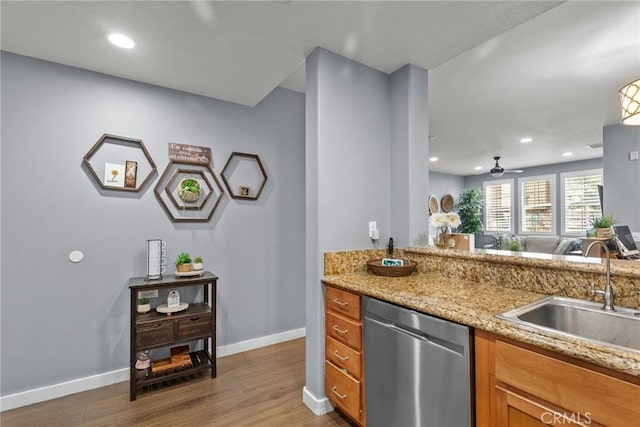 kitchen with a sink, stainless steel dishwasher, wood finished floors, brown cabinetry, and baseboards