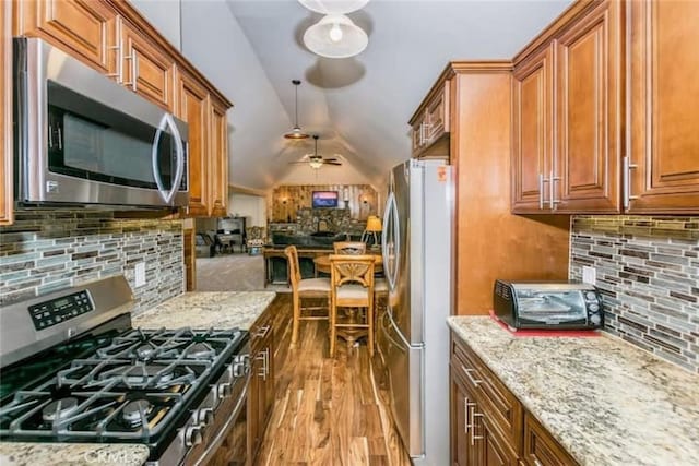 kitchen with brown cabinetry, light stone countertops, lofted ceiling, stainless steel appliances, and tasteful backsplash