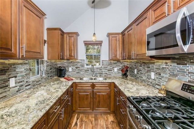 kitchen with a sink, stainless steel appliances, light stone counters, and brown cabinets