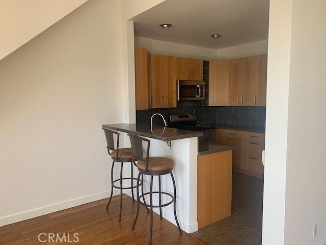 kitchen with a breakfast bar area, a peninsula, decorative backsplash, appliances with stainless steel finishes, and dark countertops