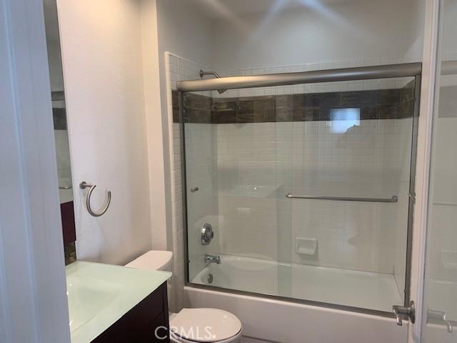 bathroom with combined bath / shower with glass door, toilet, and vanity