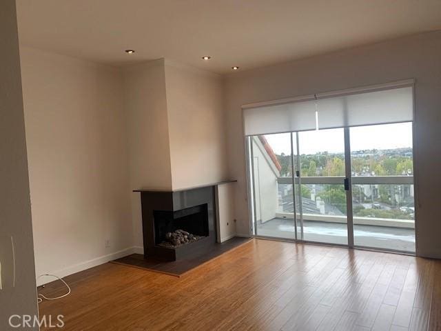 unfurnished living room featuring a multi sided fireplace, recessed lighting, baseboards, and wood finished floors