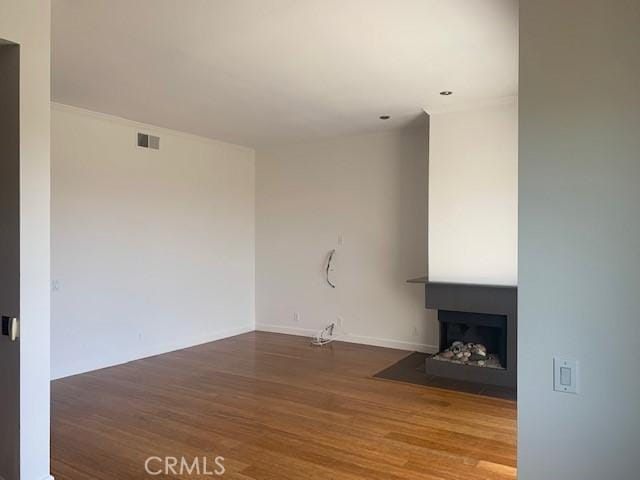 unfurnished living room featuring a fireplace with flush hearth, wood finished floors, and visible vents