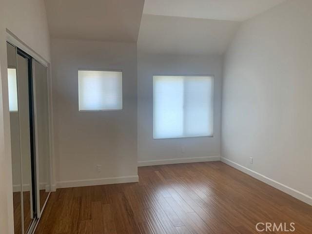 empty room featuring vaulted ceiling, baseboards, and wood finished floors