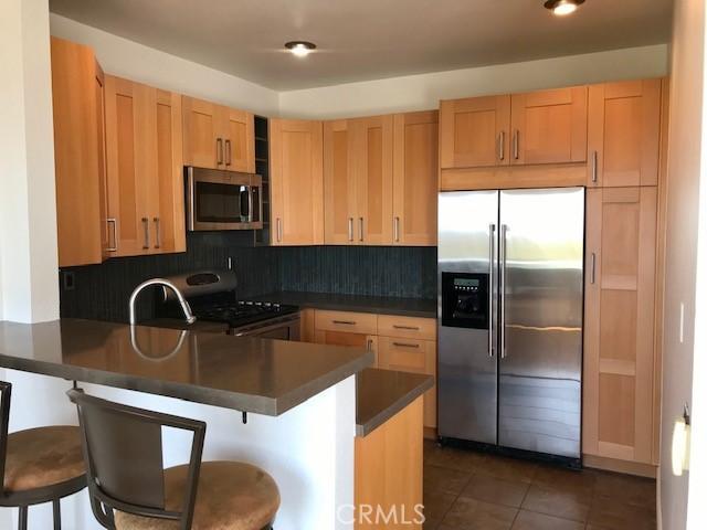 kitchen featuring dark countertops, tasteful backsplash, appliances with stainless steel finishes, a peninsula, and dark tile patterned flooring