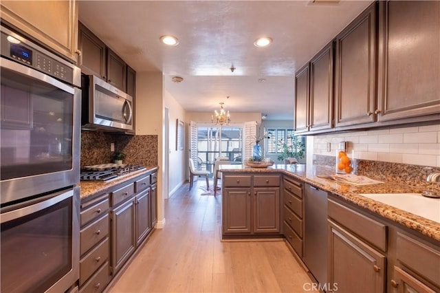 kitchen featuring light wood finished floors, tasteful backsplash, a chandelier, appliances with stainless steel finishes, and a peninsula