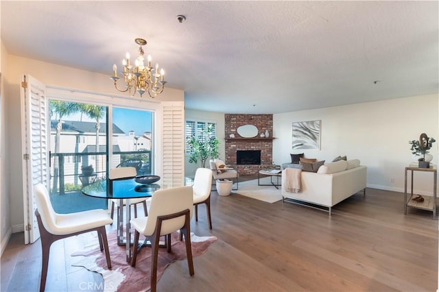 dining room with baseboards, a fireplace, an inviting chandelier, wood finished floors, and a textured ceiling