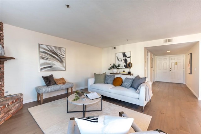 living area featuring visible vents, a brick fireplace, baseboards, and wood finished floors