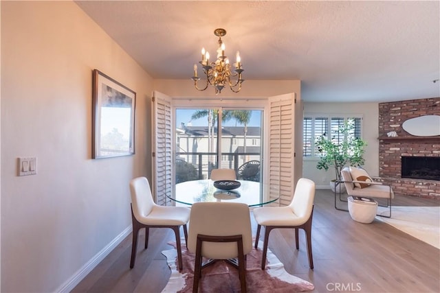 dining space featuring a notable chandelier, a fireplace, baseboards, and wood finished floors