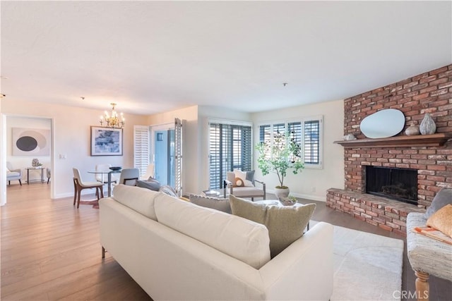 living room with a notable chandelier, a fireplace, baseboards, and wood finished floors