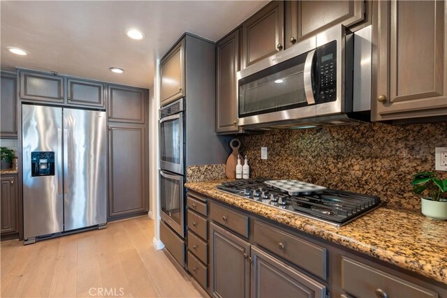 kitchen with light stone counters, light wood-style flooring, recessed lighting, stainless steel appliances, and backsplash