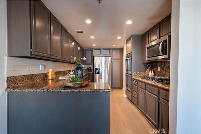 kitchen with dark stone countertops, light wood-type flooring, visible vents, and stainless steel appliances