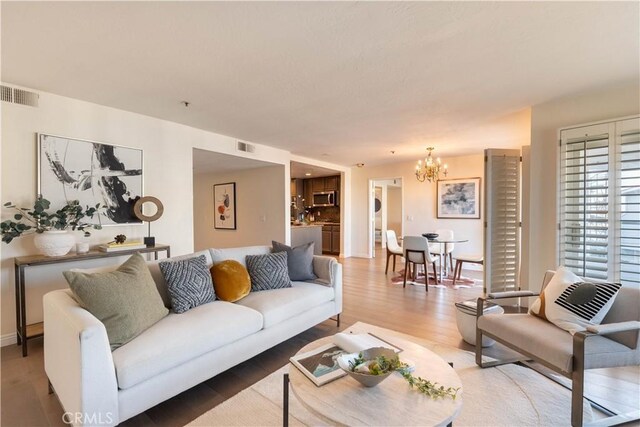 living area featuring a notable chandelier, visible vents, and light wood-type flooring