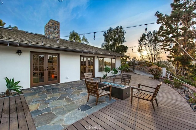 deck at dusk featuring french doors and a fire pit