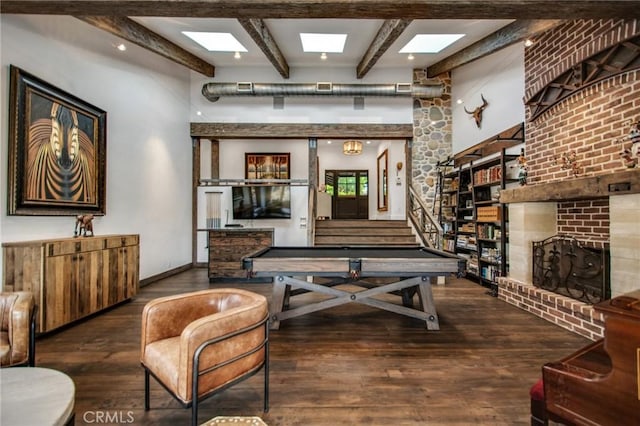 playroom with baseboards, beam ceiling, a skylight, hardwood / wood-style flooring, and a brick fireplace