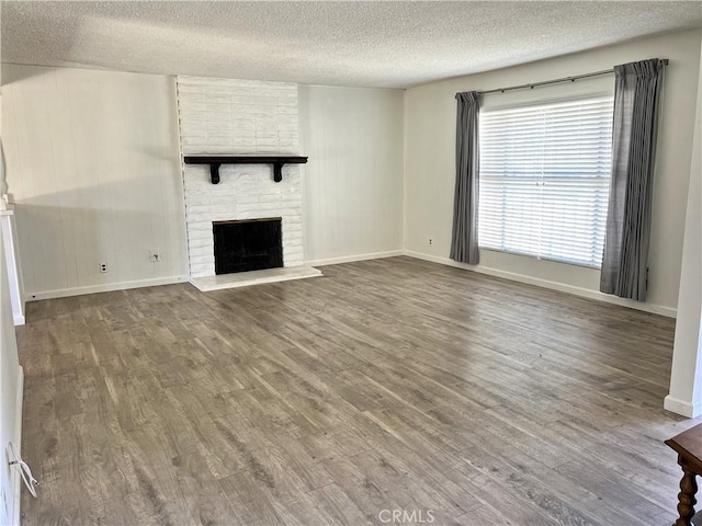 unfurnished living room featuring a brick fireplace, a textured ceiling, baseboards, and wood finished floors