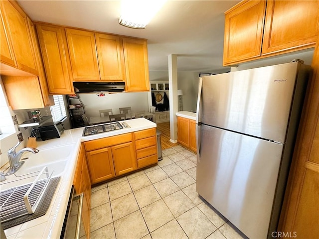 kitchen with extractor fan, light countertops, light tile patterned floors, freestanding refrigerator, and gas stovetop