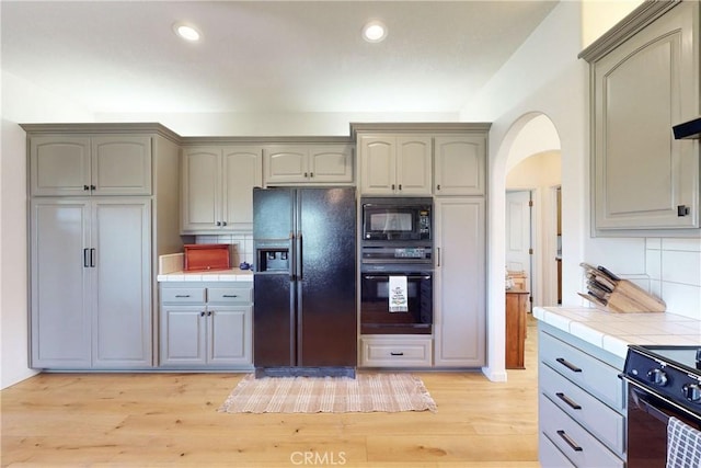 2139 Verde Canyon Rd, Arroyo Grande, CA 93420 - kitchen with black appliances, tile countertops, arched walkways, light wood-style flooring, and decorative backsplash