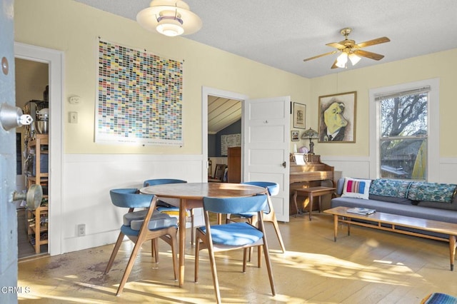 dining space with a ceiling fan, wood finished floors, a wainscoted wall, and a textured ceiling