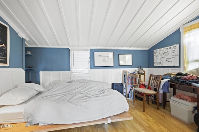 bedroom with vaulted ceiling, wood finished floors, and a wainscoted wall