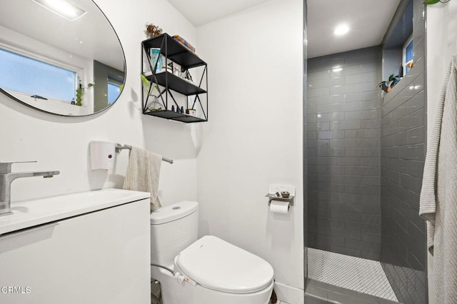 bathroom with a tile shower, toilet, and vanity