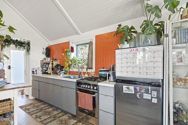 kitchen with gray cabinetry, vaulted ceiling with beams, wood ceiling, stainless steel appliances, and a sink