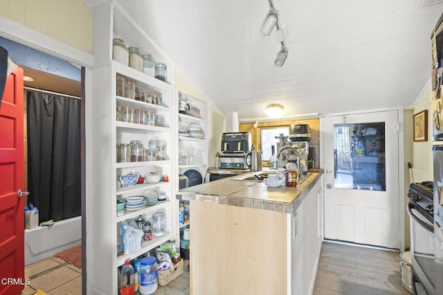 kitchen featuring track lighting, a sink, wood finished floors, gas range oven, and tile counters