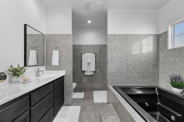 bathroom with a jetted tub, a wainscoted wall, toilet, vanity, and tile walls