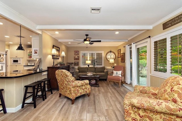 living area with light wood-type flooring, beamed ceiling, ornamental molding, and a ceiling fan