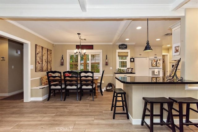 kitchen featuring white appliances, a breakfast bar, light wood-style flooring, dark countertops, and beamed ceiling