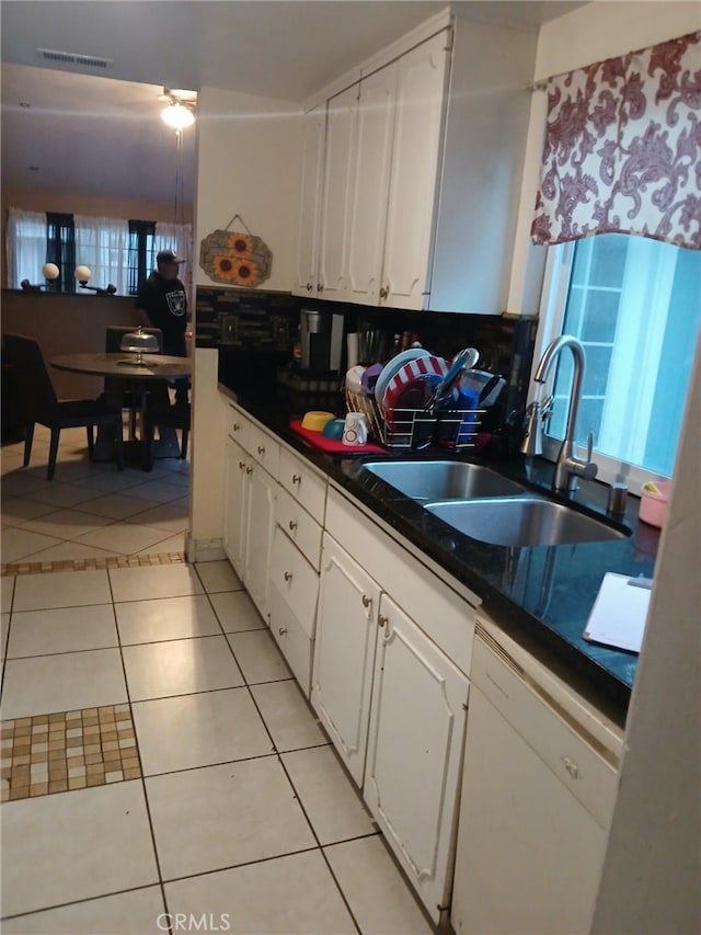 kitchen with dark countertops, light tile patterned floors, white dishwasher, white cabinetry, and a sink