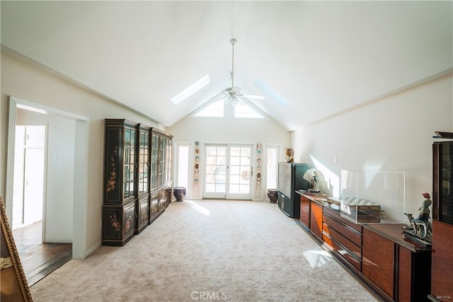 living room with a skylight, light colored carpet, french doors, and high vaulted ceiling