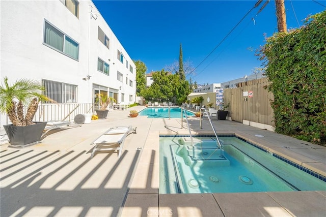 community pool with a patio area, fence, and a hot tub